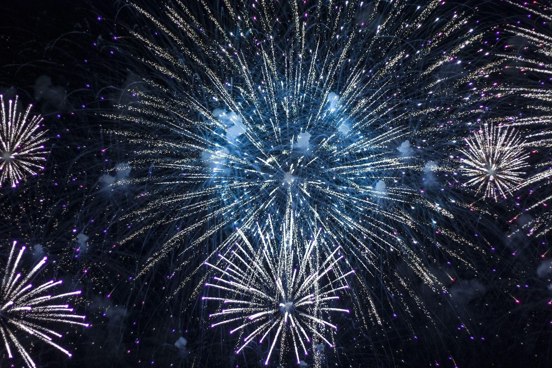 Fireworks bursting brightly in a dark night sky; white and blue sparks.
