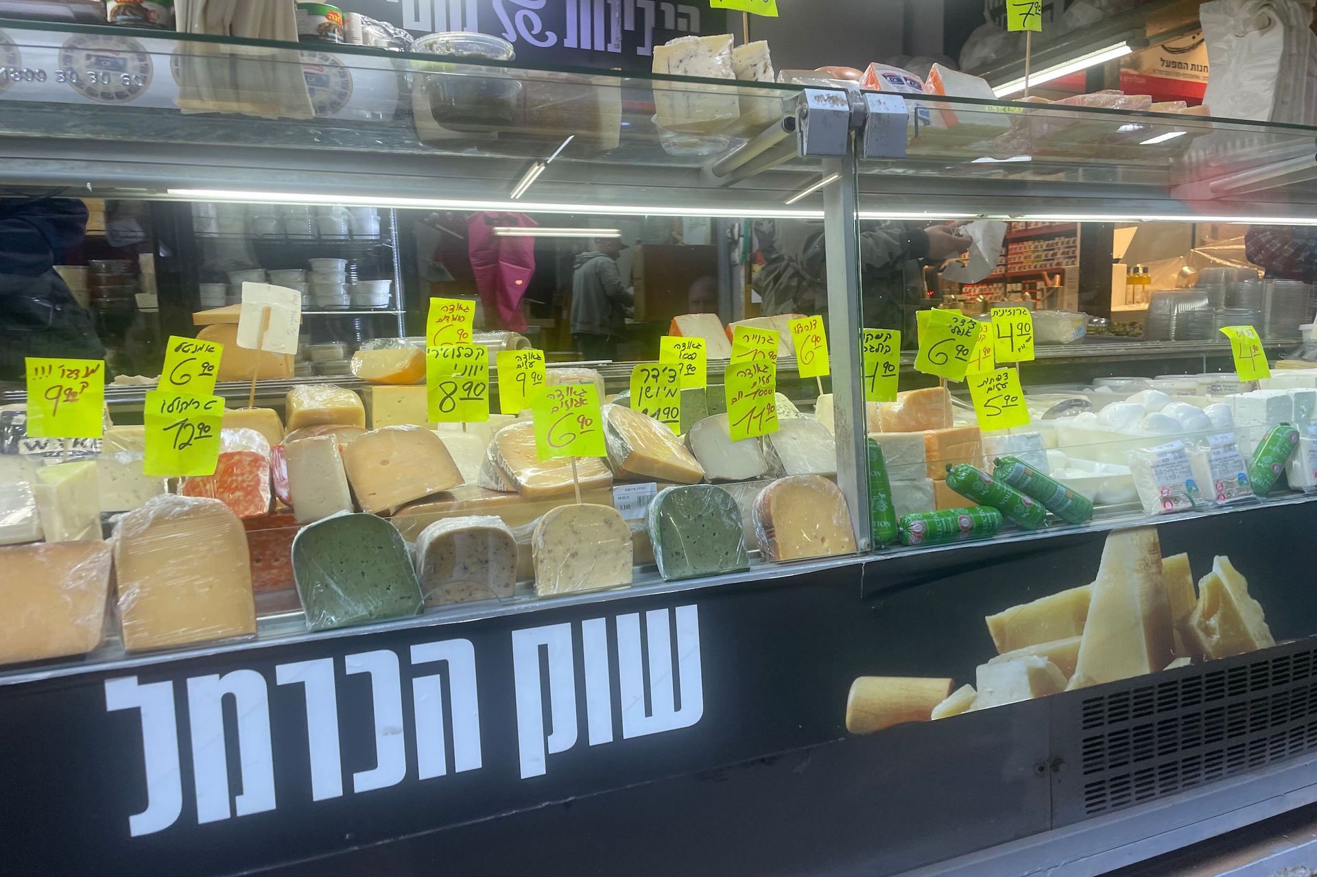 Cheese display at a Carmel Market stall, with various types and yellow price tags.