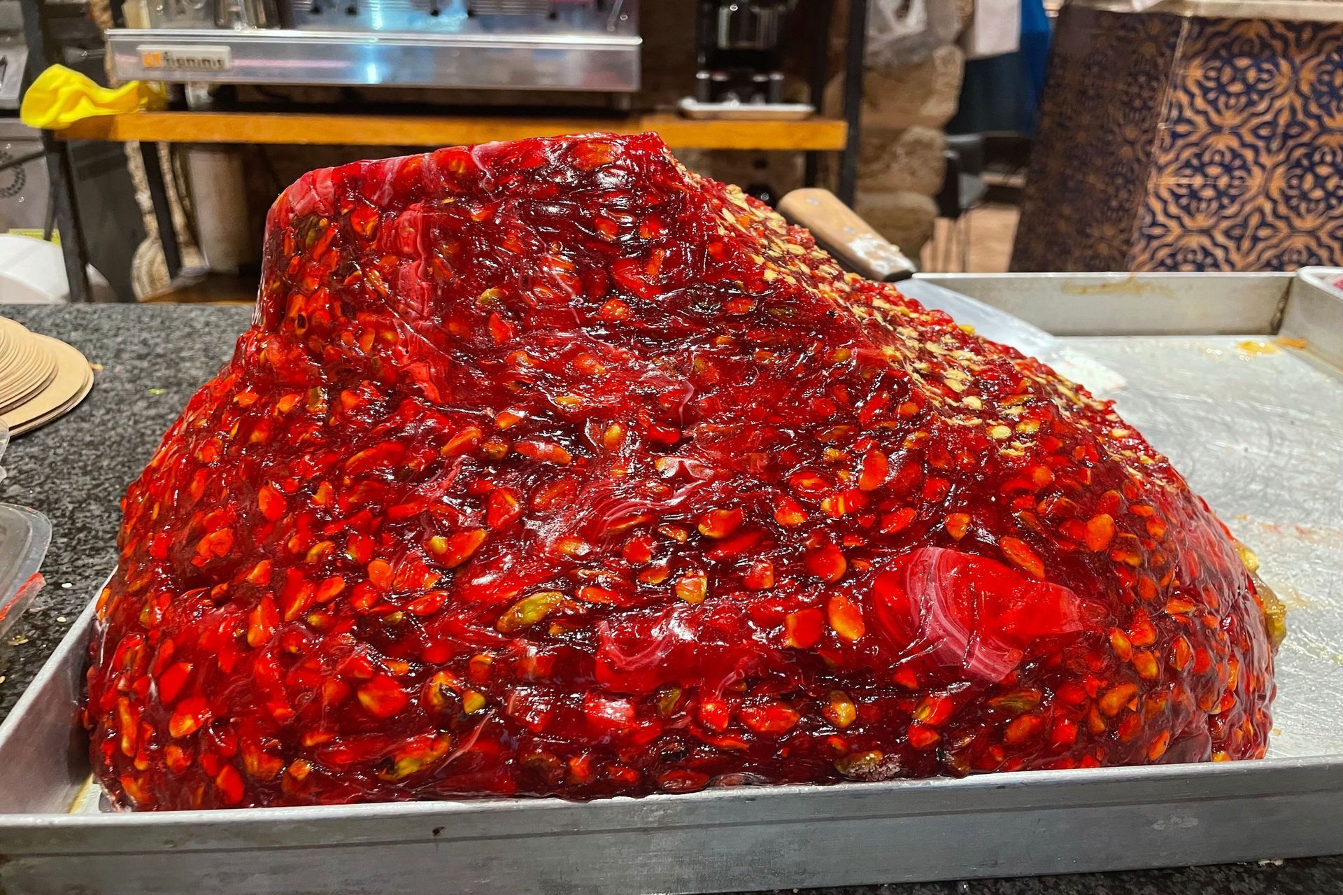 Large, red, jelly-like dessert studded with nuts on a metal tray.