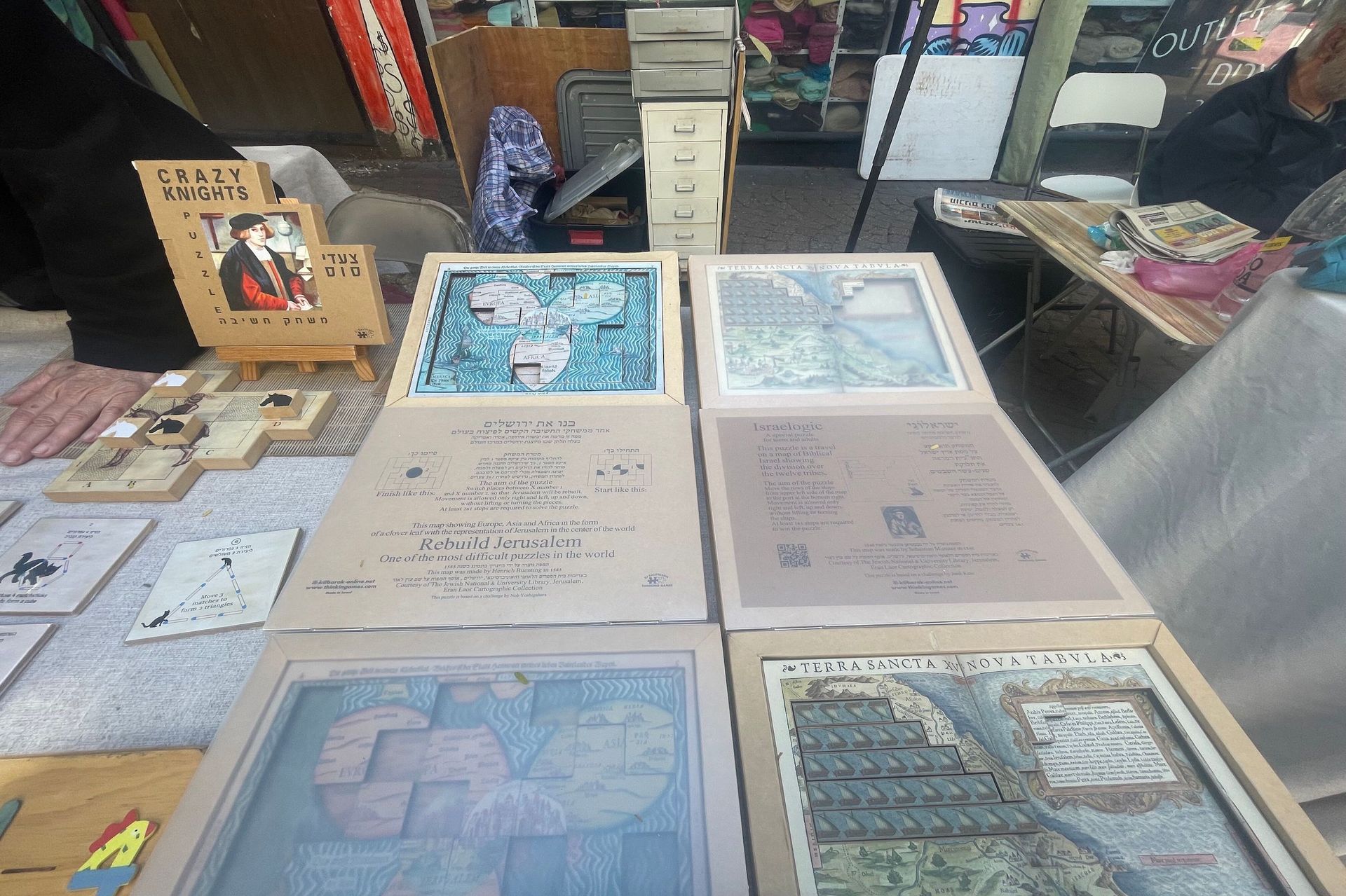 Artwork display at an outdoor market: framed art on a table. A sign says 