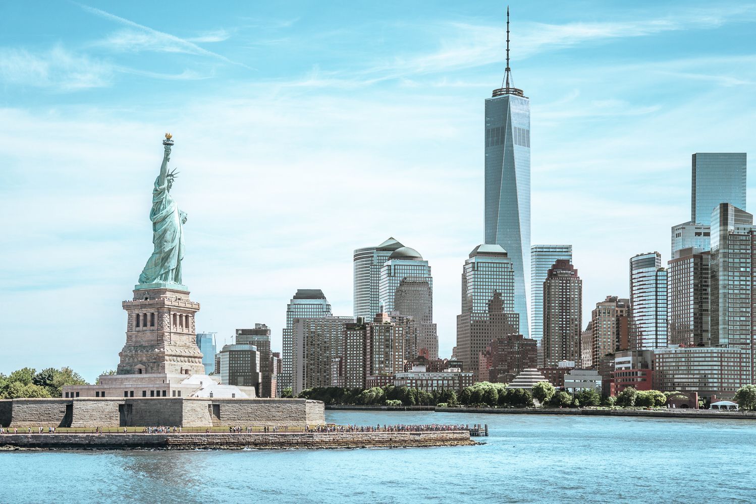 Statue of Liberty stands in front of the New York City skyline on a sunny day.
