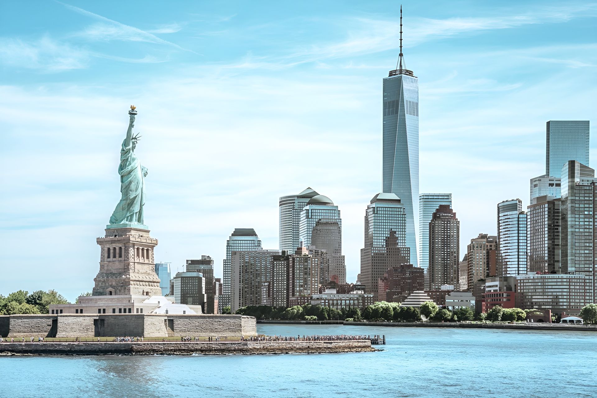 Statue of Liberty with New York City skyline; blue sky, water.
