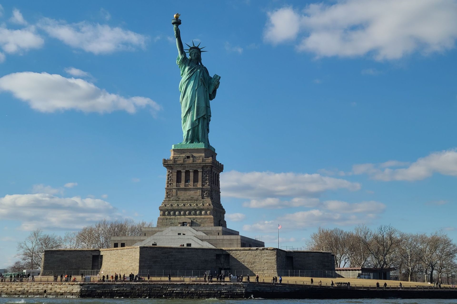 Statue of Liberty against a blue sky. Green copper statue on stone pedestal in New York Harbor.