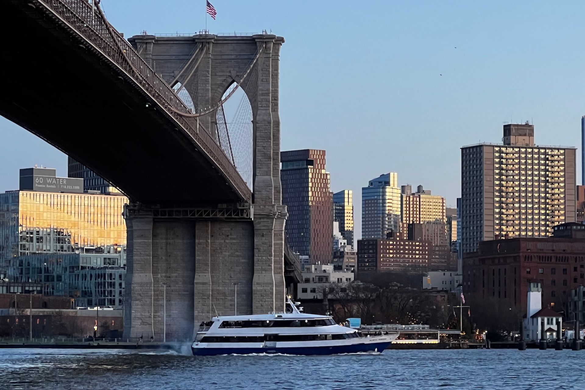Brooklyn Bridge with a ferry boat sailing below; city buildings in the background.