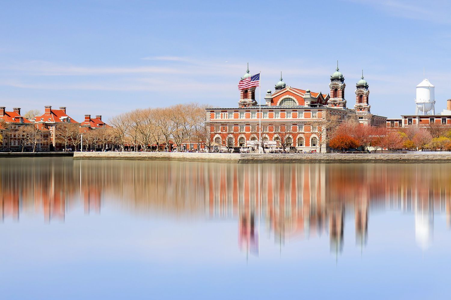 Waterfront building with a red brick facade, American flag, and clear reflections in calm water.