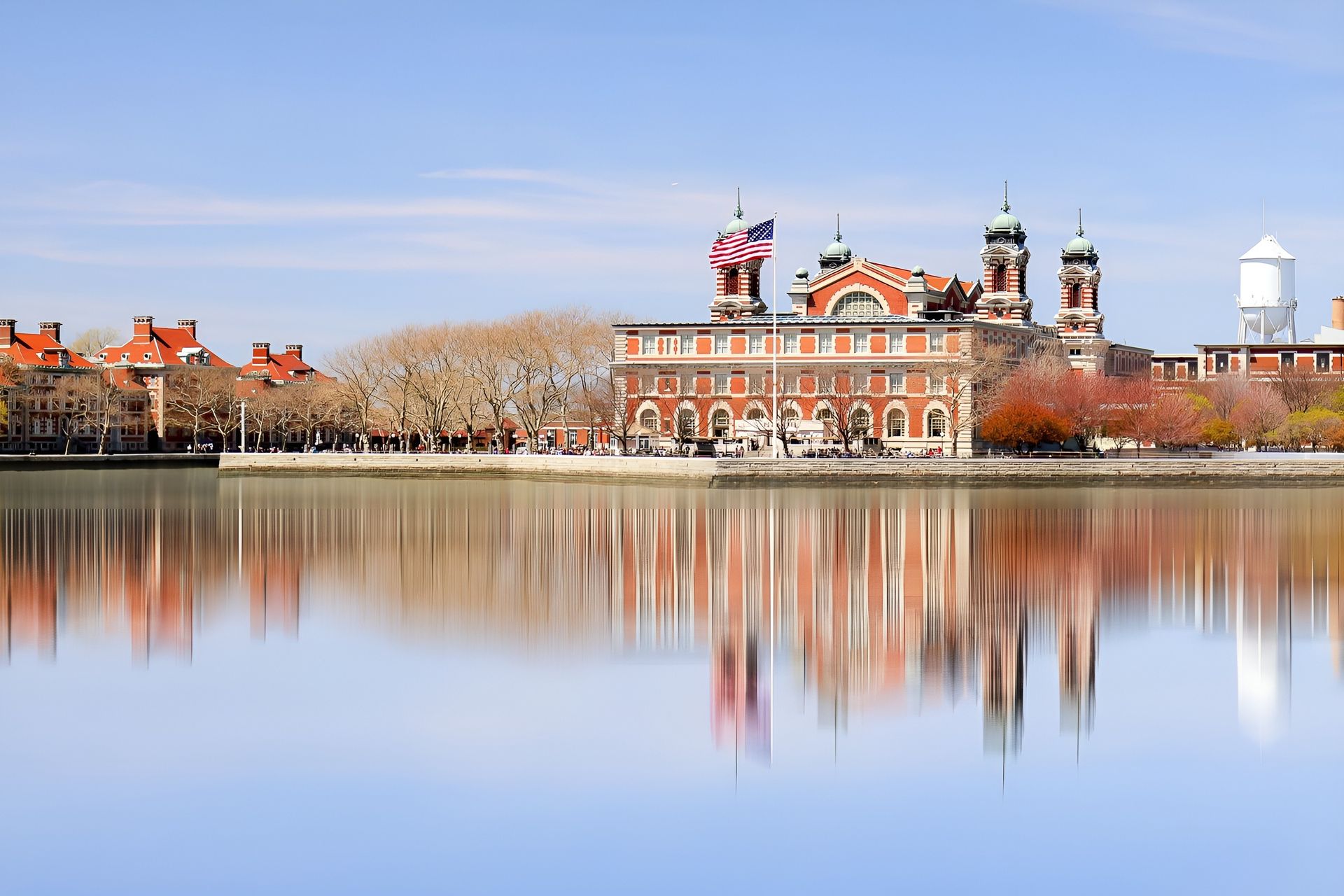Brick building with two domes reflected in water, under a blue sky.