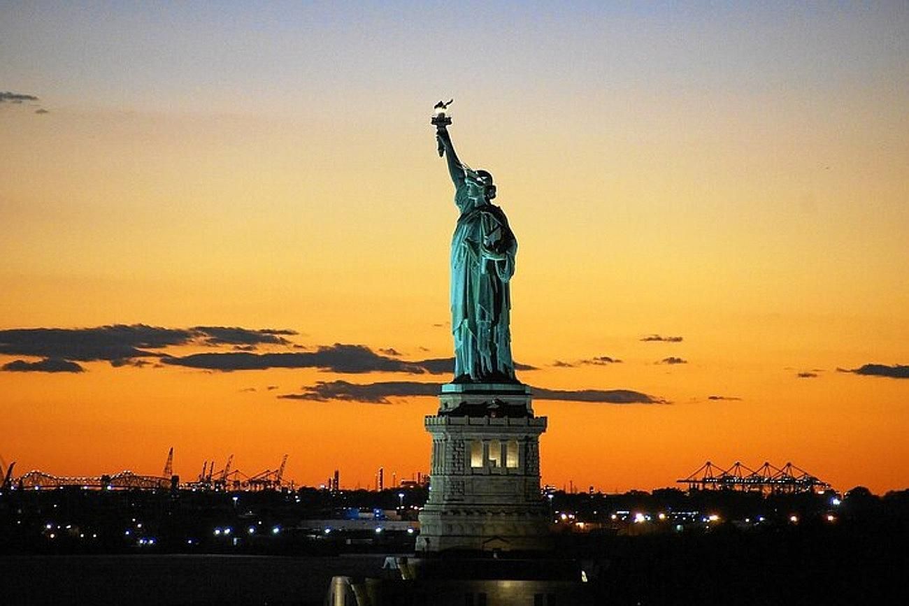 Statue of Liberty silhouetted against an orange and yellow sunset.