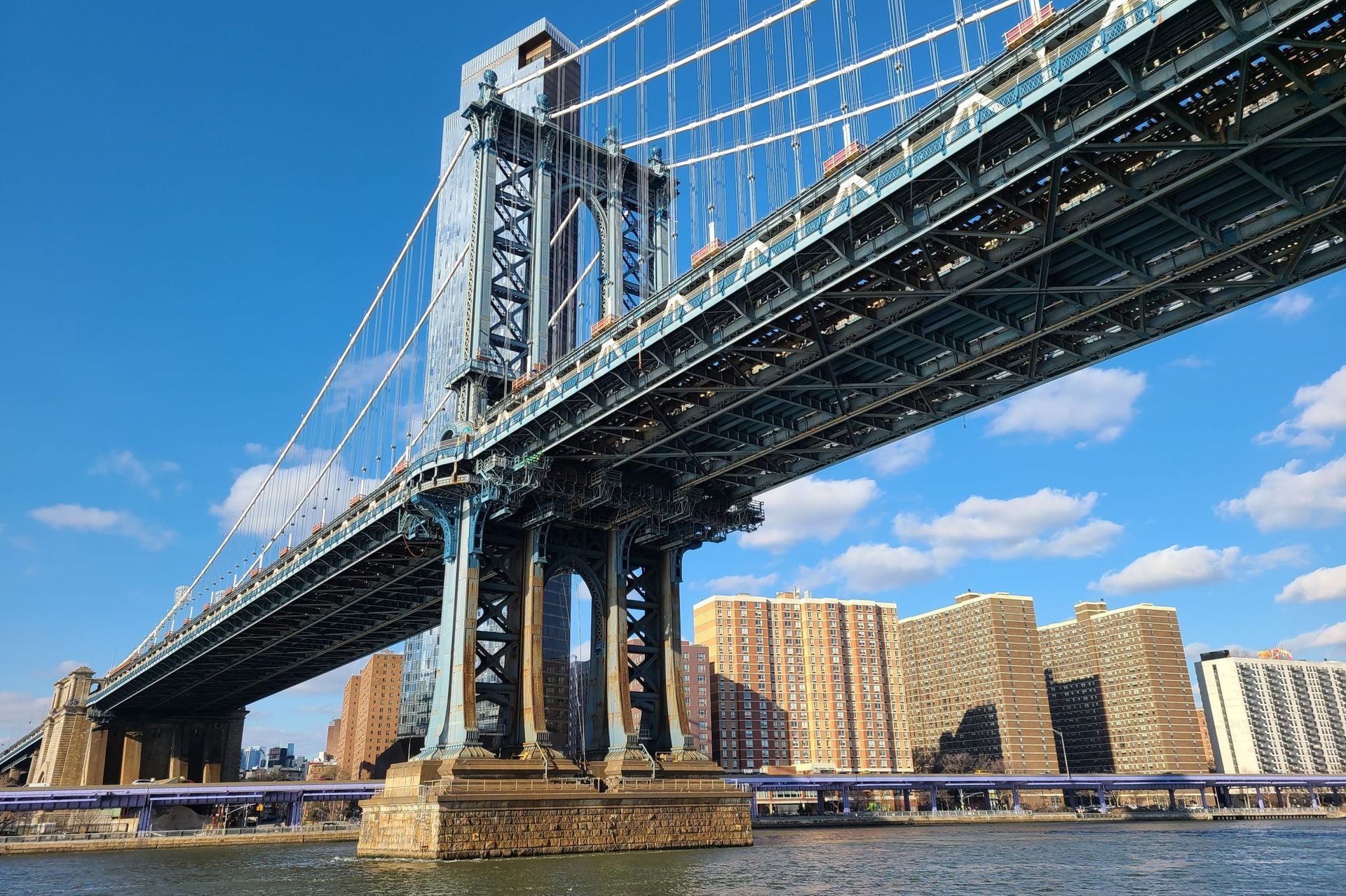 Manhattan Bridge against a clear blue sky with city buildings visible in the background.
