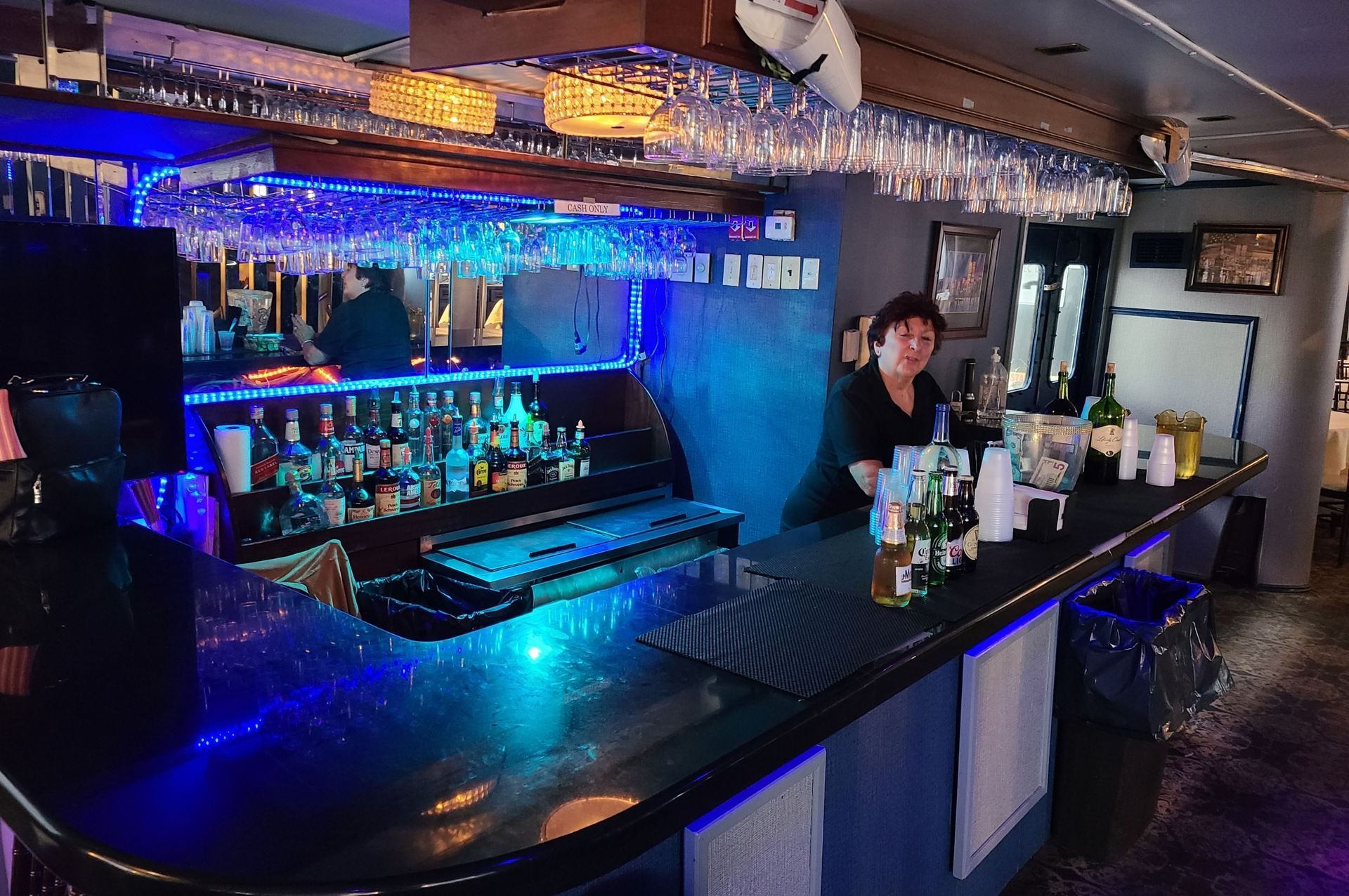 Bar with a bartender, blue lights, bottles, and hanging glasses.