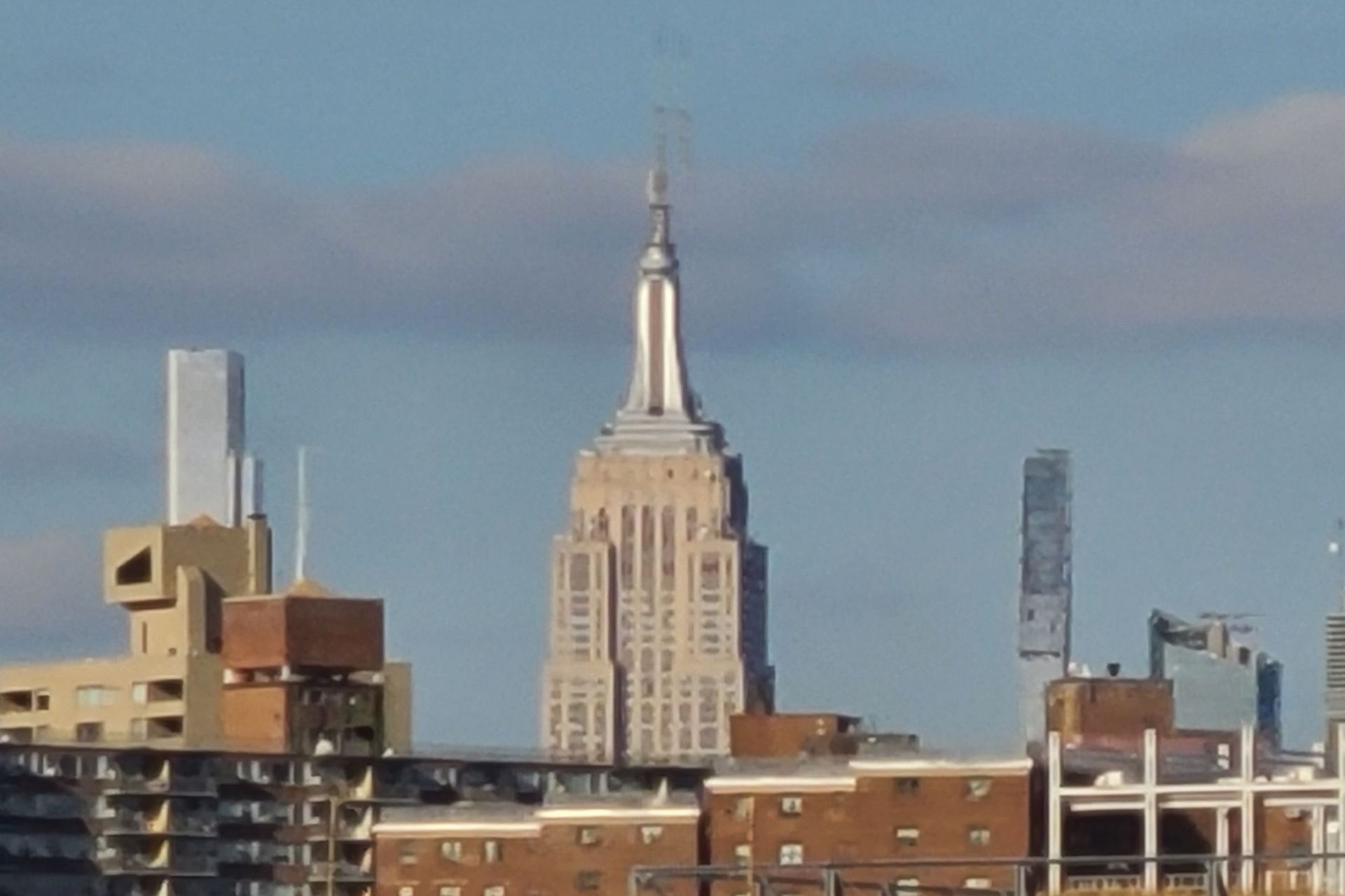 Empire State Building towering above other buildings, against a cloudy sky.