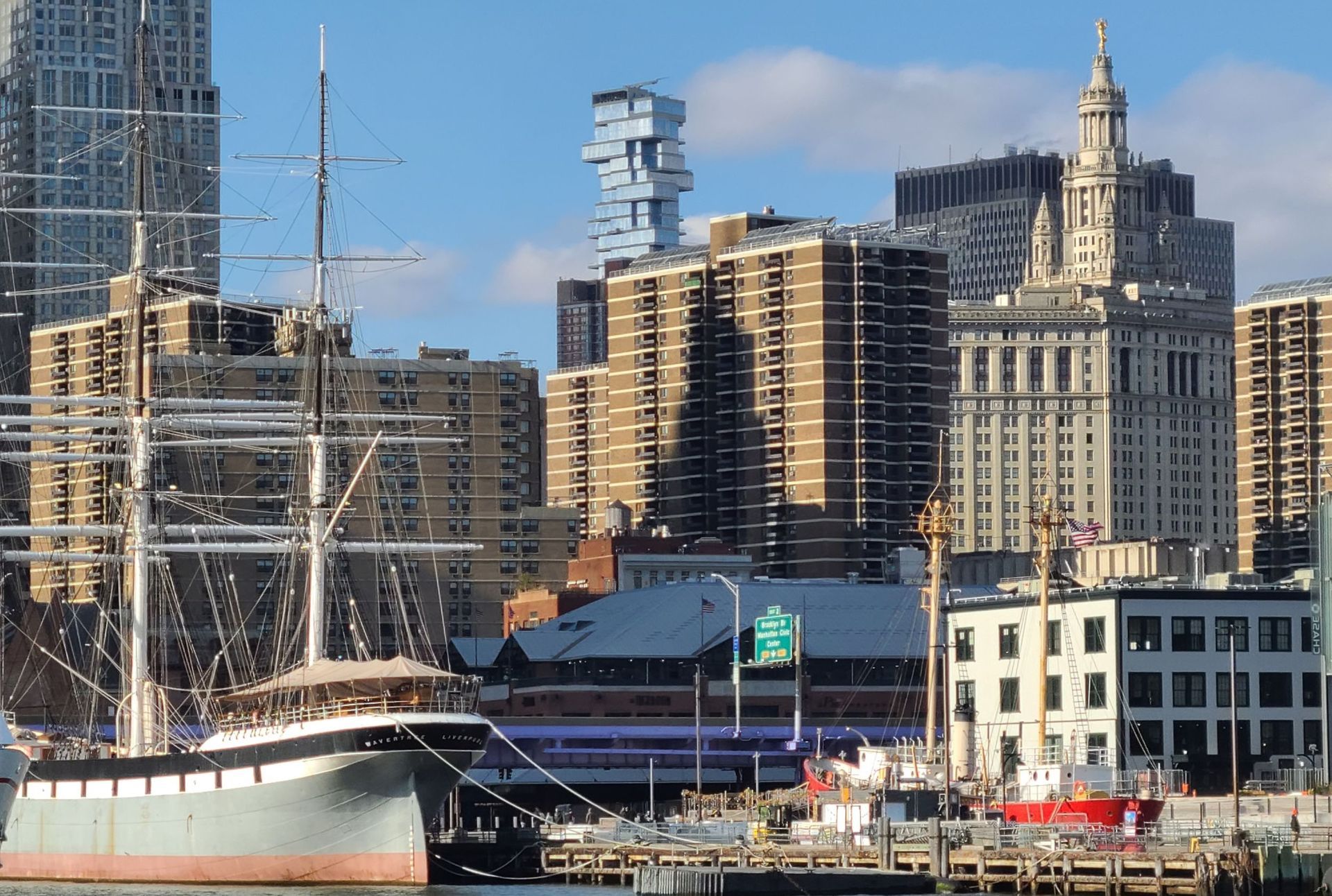 Tall ship docked in harbor with NYC skyline background.