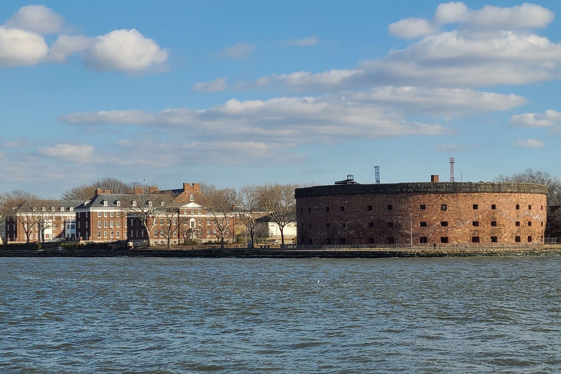 View of Fort Wadsworth and surrounding buildings on the water, under a blue sky with fluffy clouds.