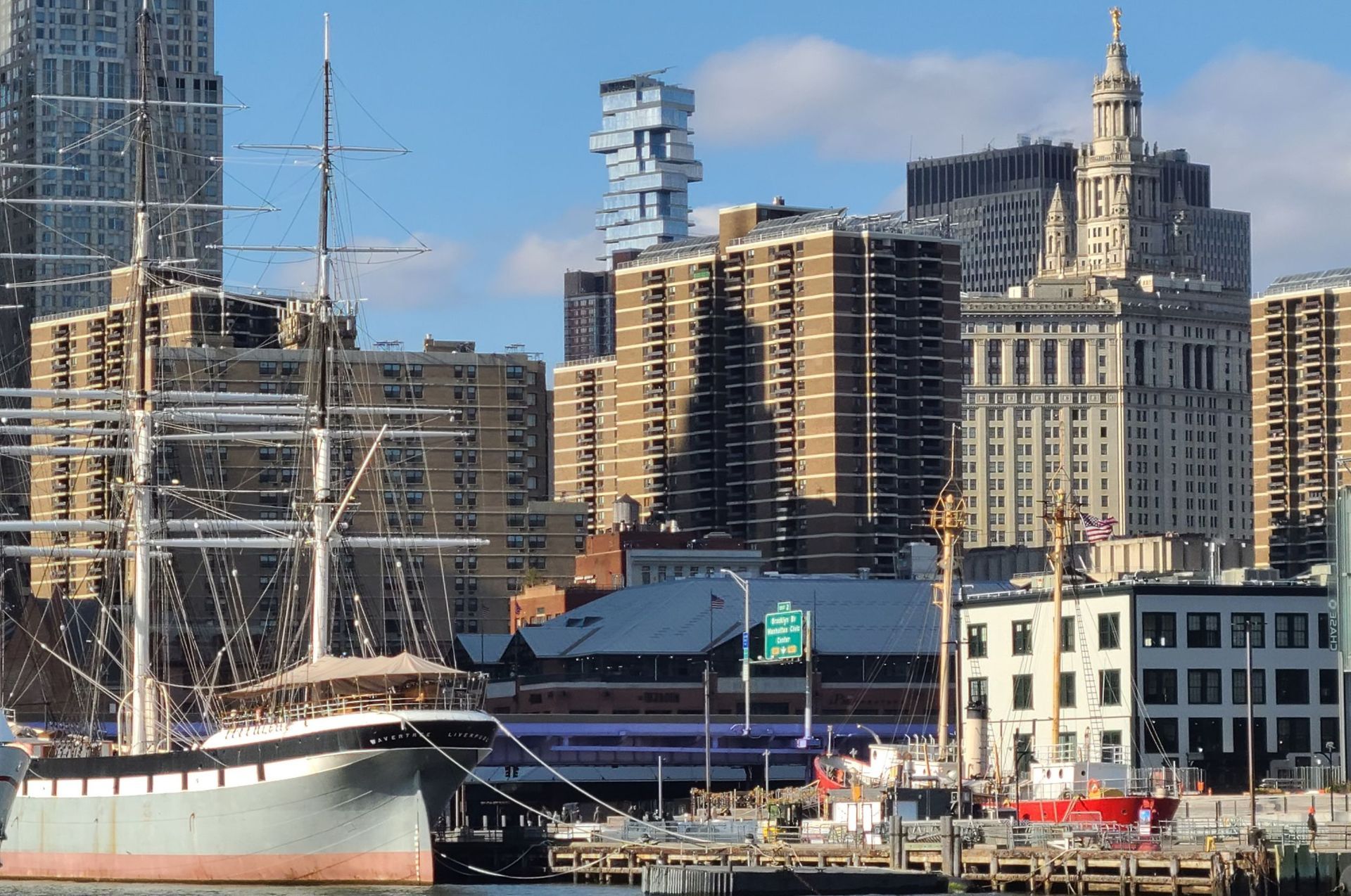 Tall ship docked in harbor, city skyline in background. Blue sky, sunny day.