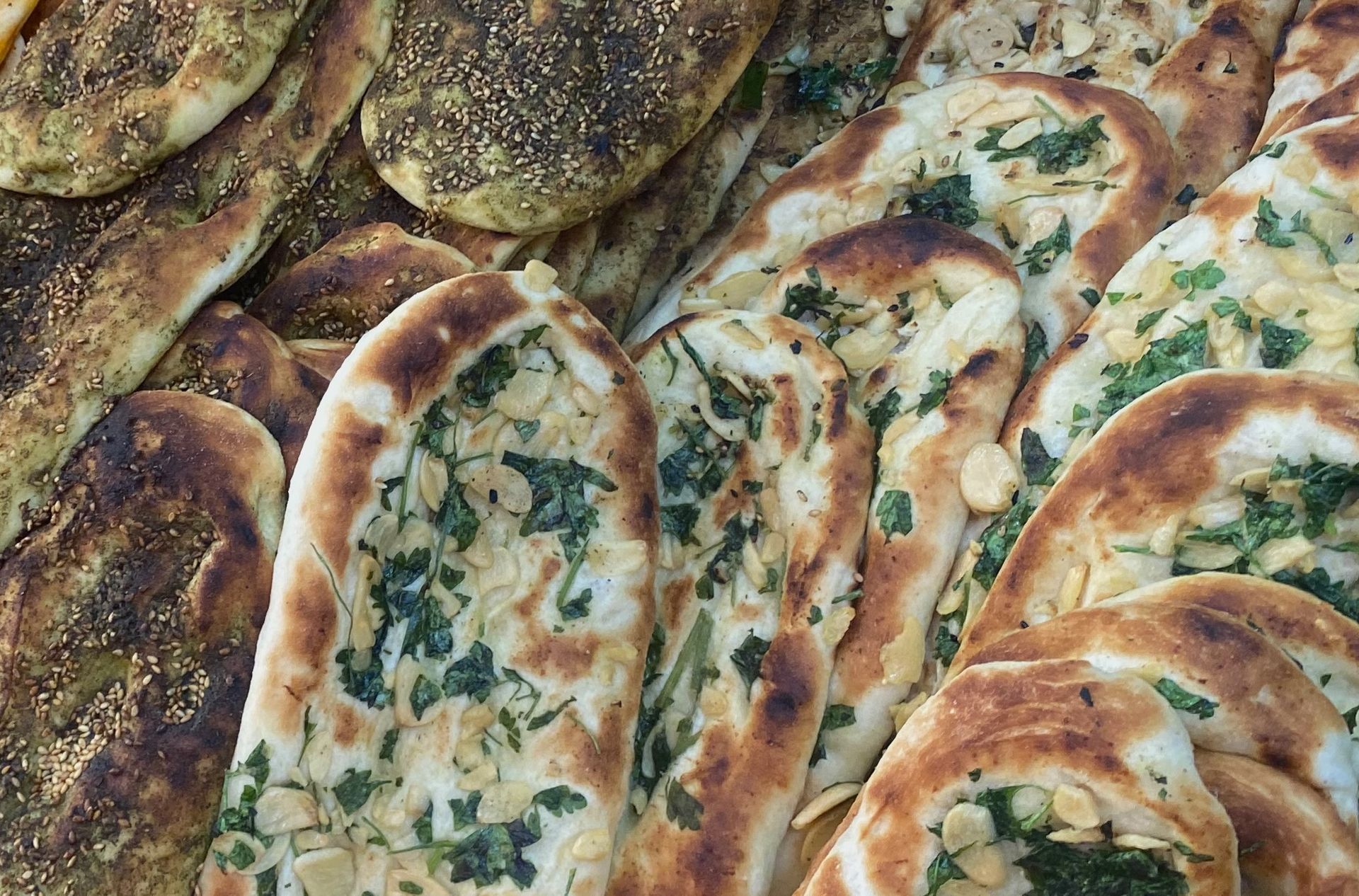 Close-up of assorted flatbreads, some topped with herbs and nuts, others with a spice mix.