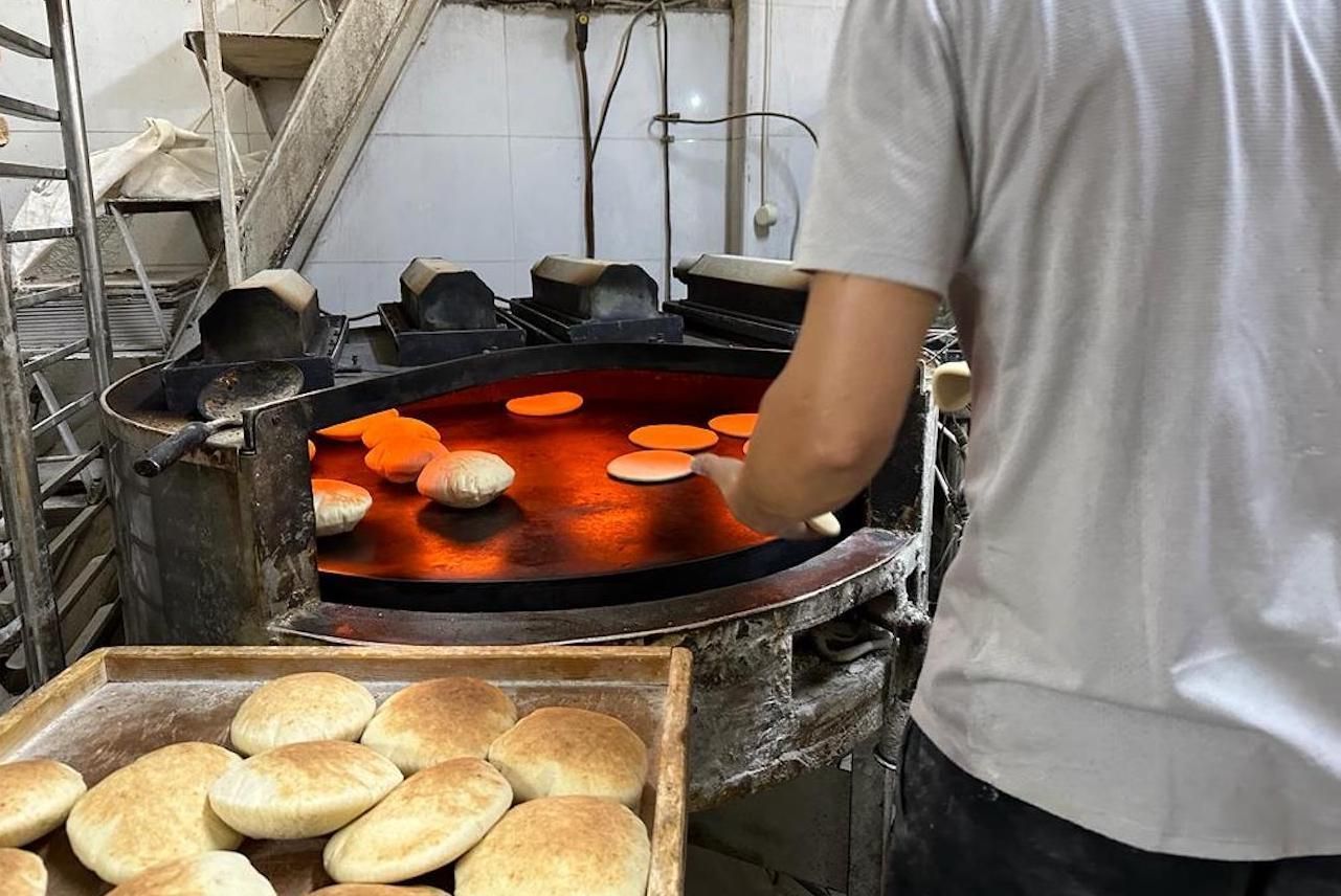 Man baking pita bread in a commercial oven. Tray of baked bread in the foreground.
