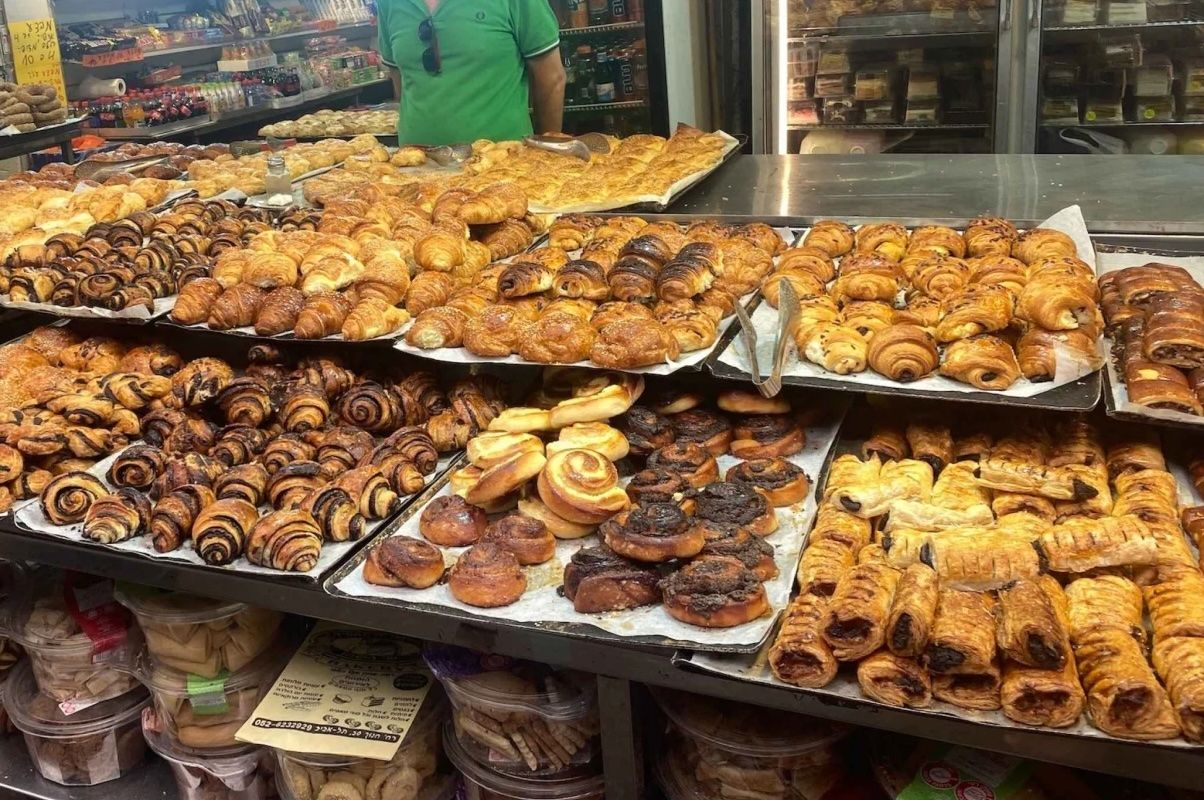 Bakery display with various pastries: croissants, rolls, and swirls; person in green shirt in the background.