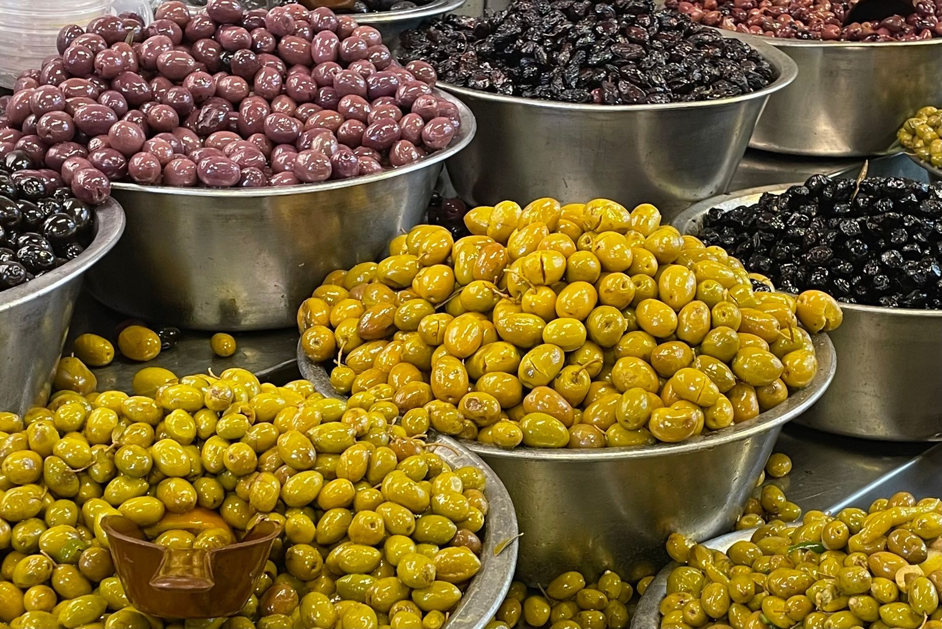 Assorted olives in metal bowls at a market, showcasing various colors like green, purple, and black.