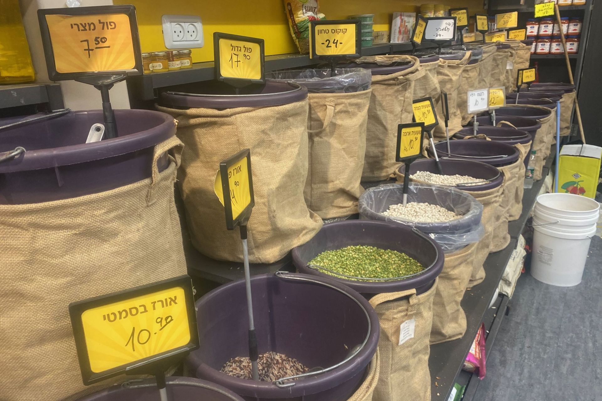 Bags of grains and legumes in a shop, with price tags in Hebrew.