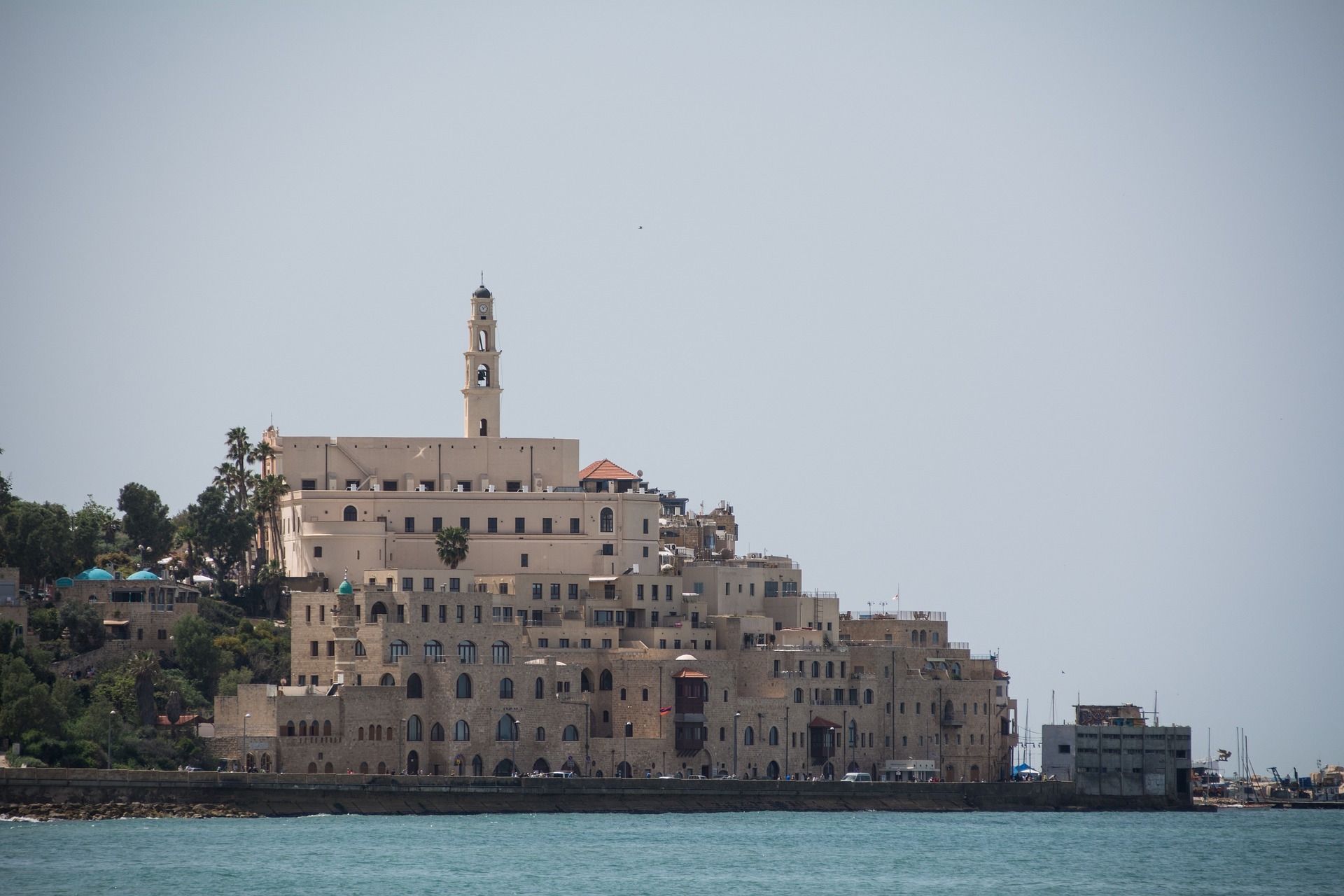Stone buildings with a tower on a seaside hill, against a light blue sky.