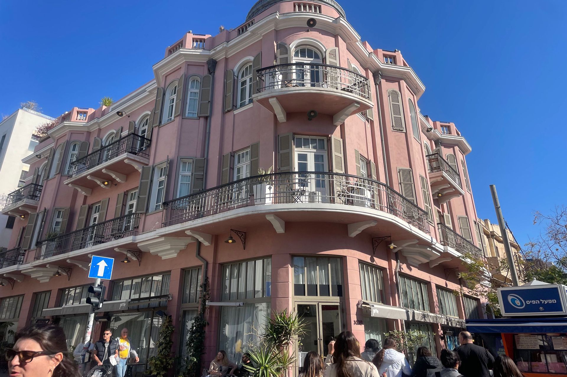Pink historic building with balconies, corner view, pedestrians on street.