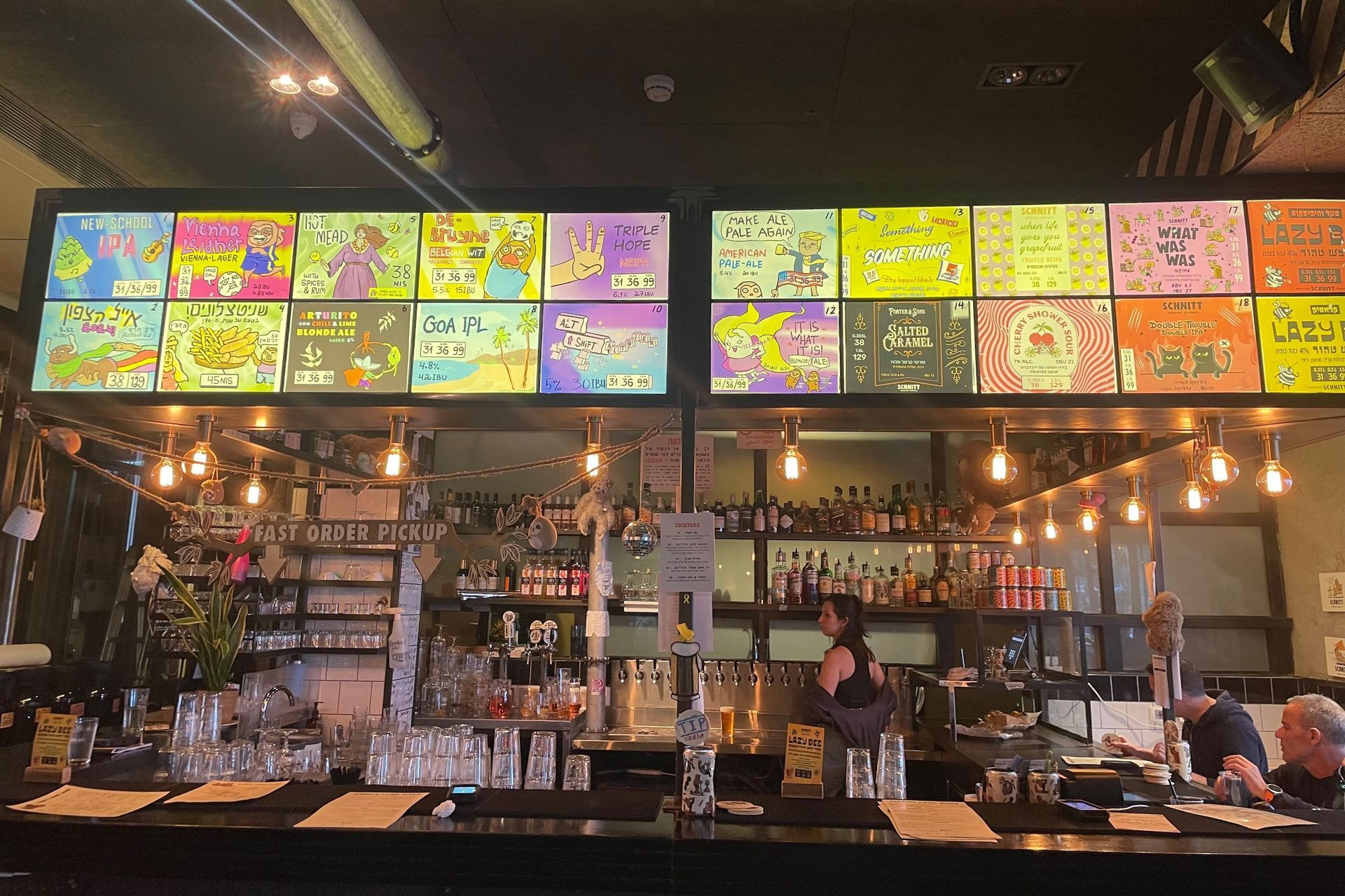 A bar interior with overhead menu boards, bartenders, and customers at the counter.