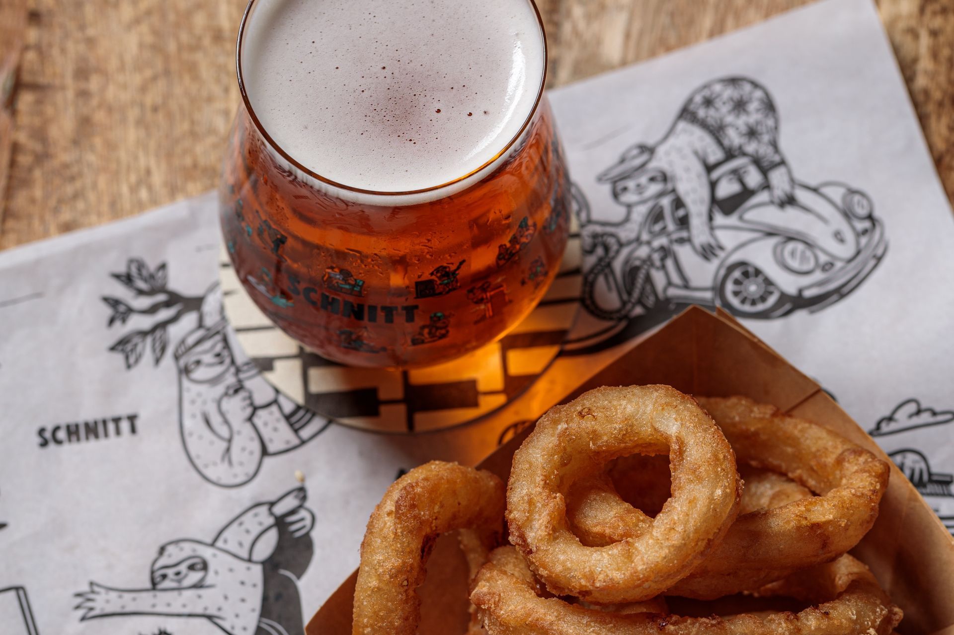 Beer glass and onion rings on a paper with a cartoon sloth.