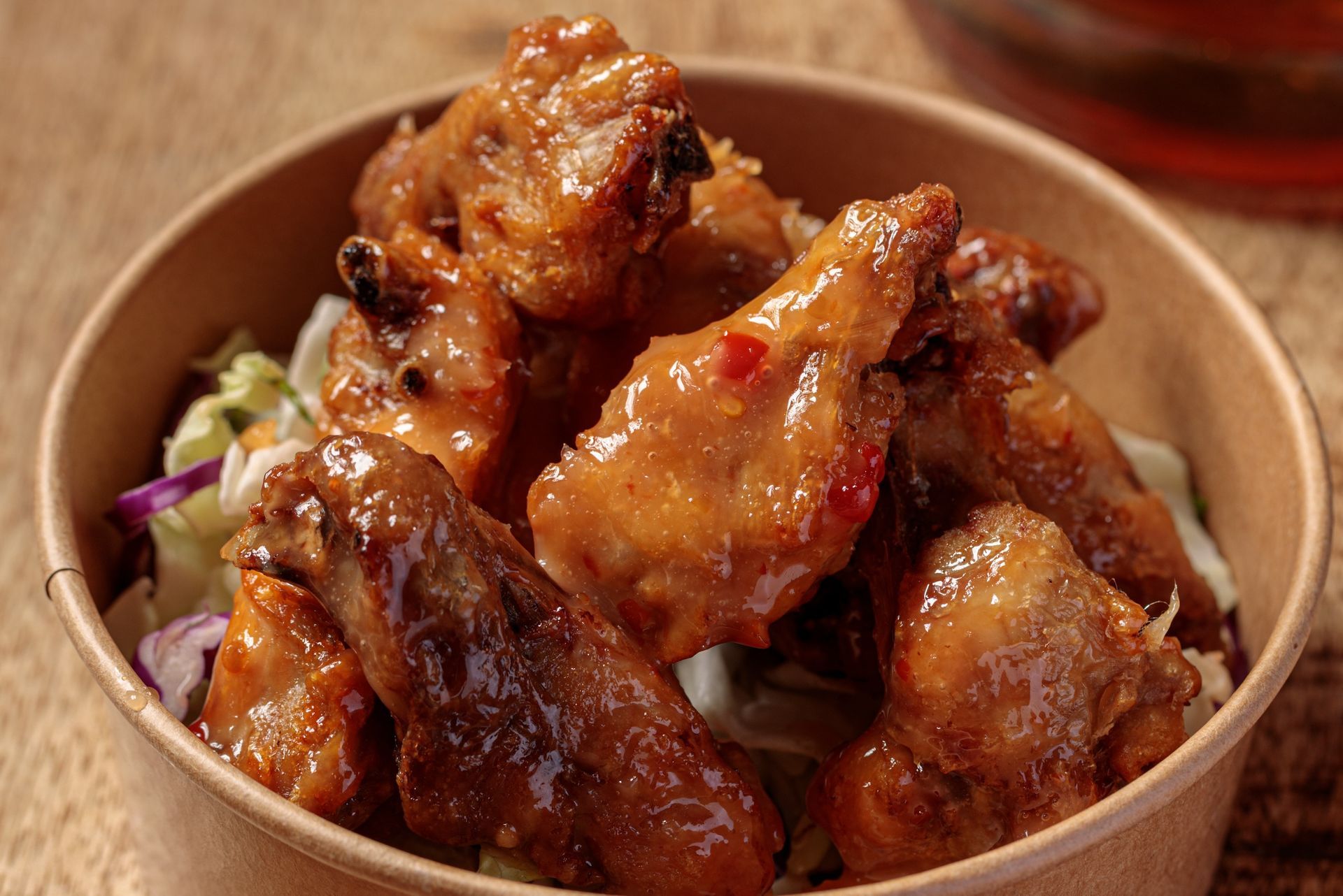 Chicken wings in a bowl, glazed with sauce, resting on coleslaw, brown and red tones.