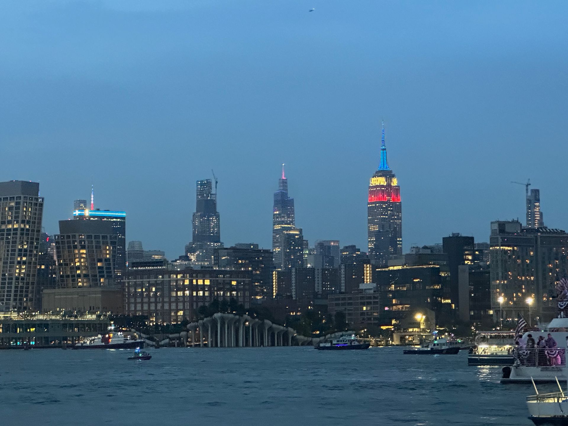 New York City skyline at dusk with illuminated buildings, including the Empire State Building in red, white, and blue.