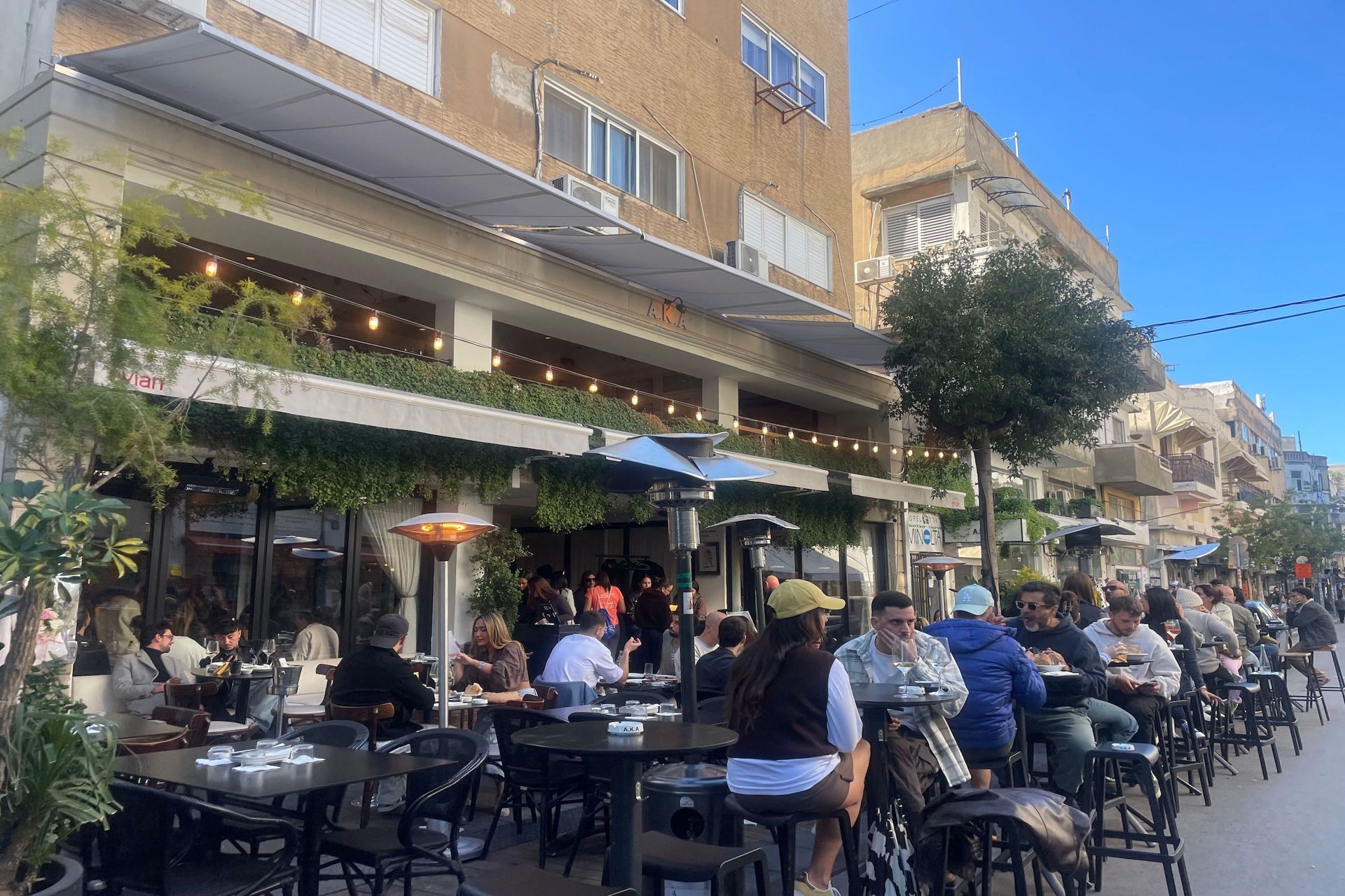 A crowded outdoor cafe with people sitting at tables, enjoying food and drinks.