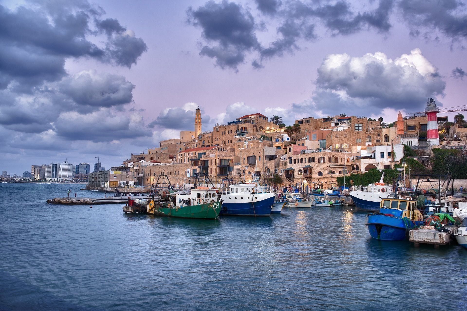 Boats in harbor at sunset, old buildings on a hill, a red and white lighthouse, Tel Aviv, Israel.