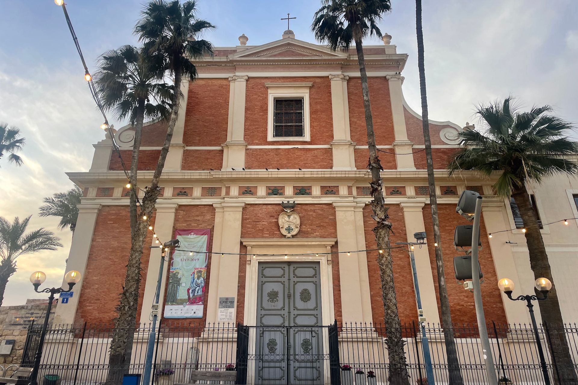 A red brick church with a detailed facade and palm trees in Jaffa, Israel, at dusk.