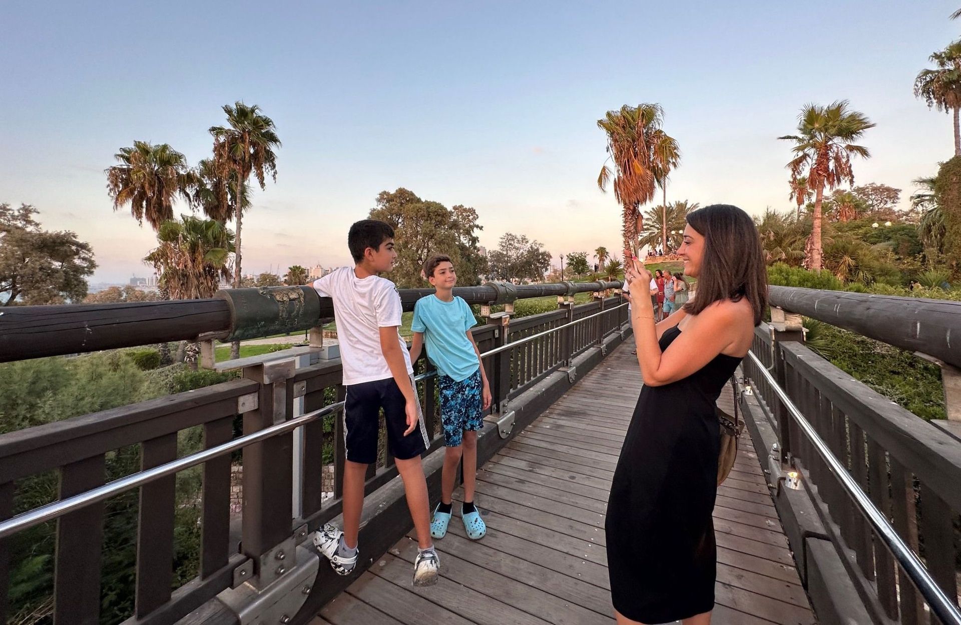 Woman taking photo of two boys on wooden bridge with palm trees.