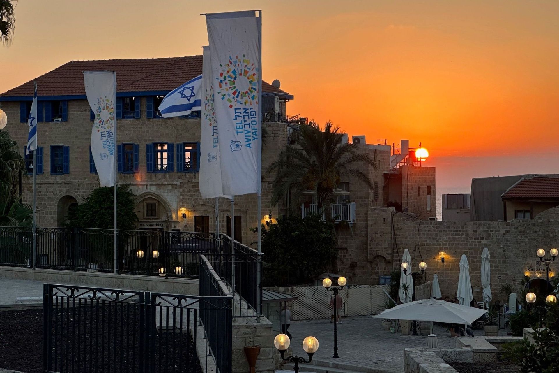Sunset over an old stone building with blue shutters and Israeli flags.