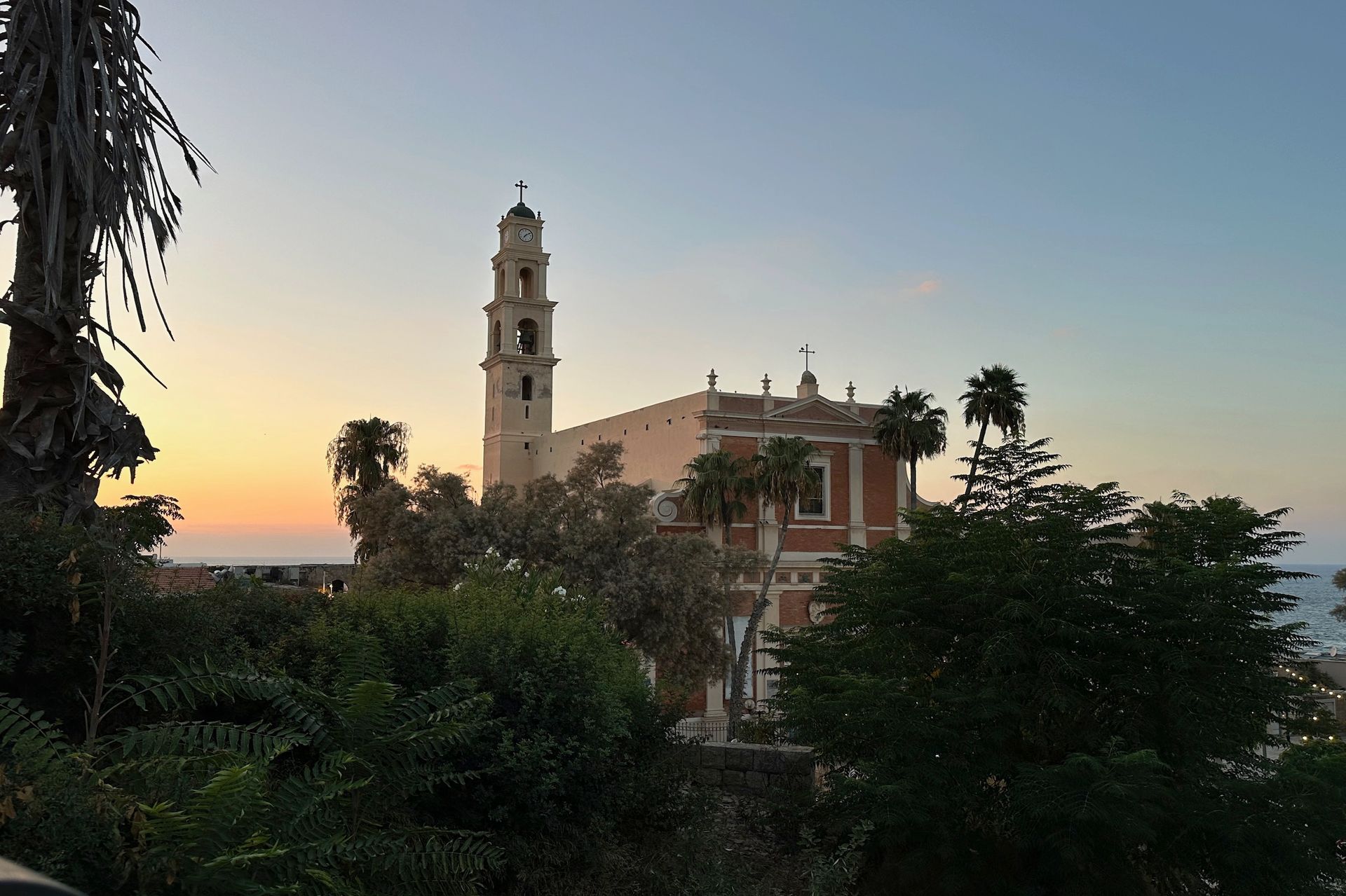 Sunset view of a church in Jaffa, Israel. Tower and palm trees against a colorful sky.