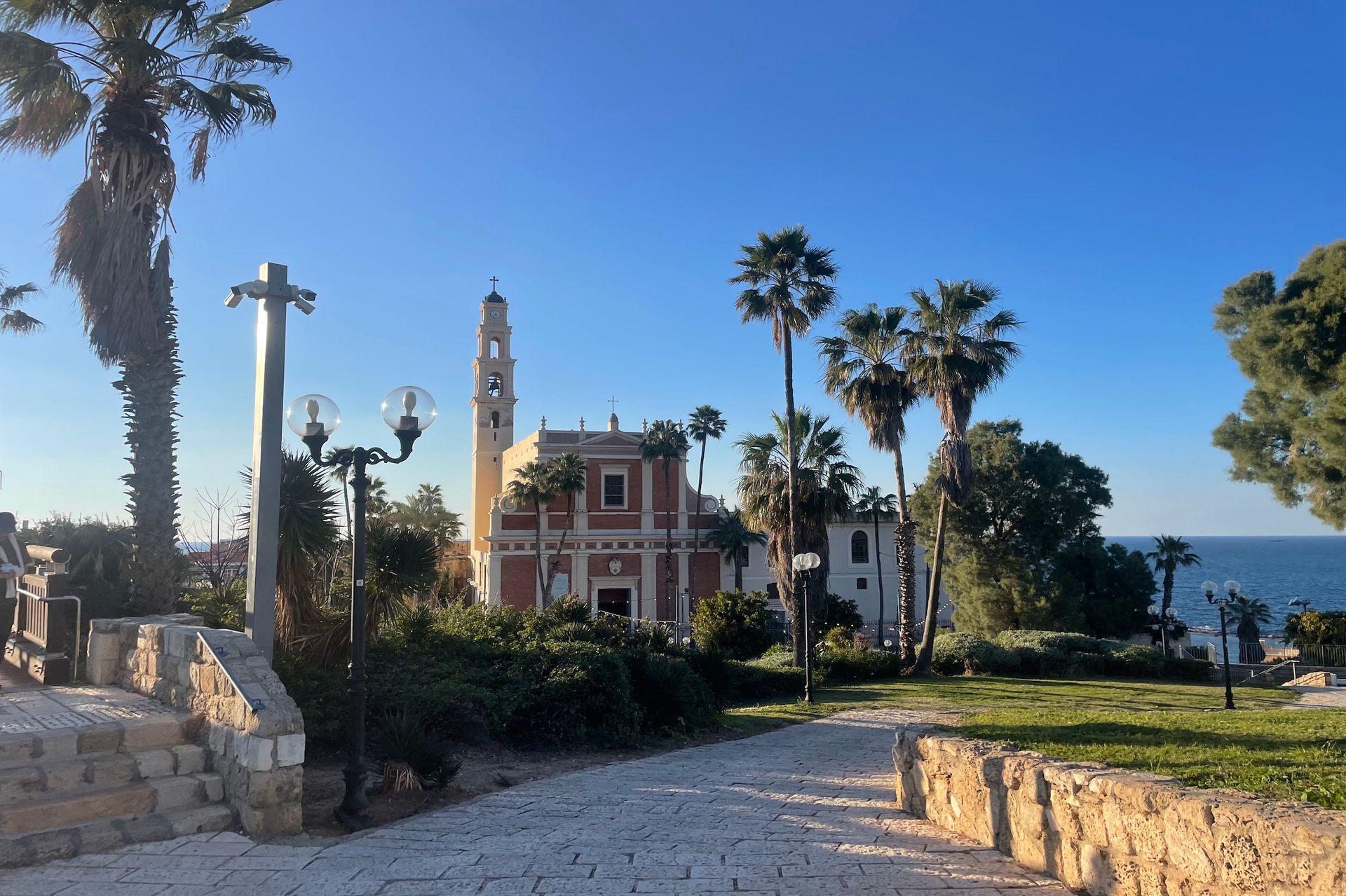 Church with bell tower and palm trees by the sea on a sunny day.