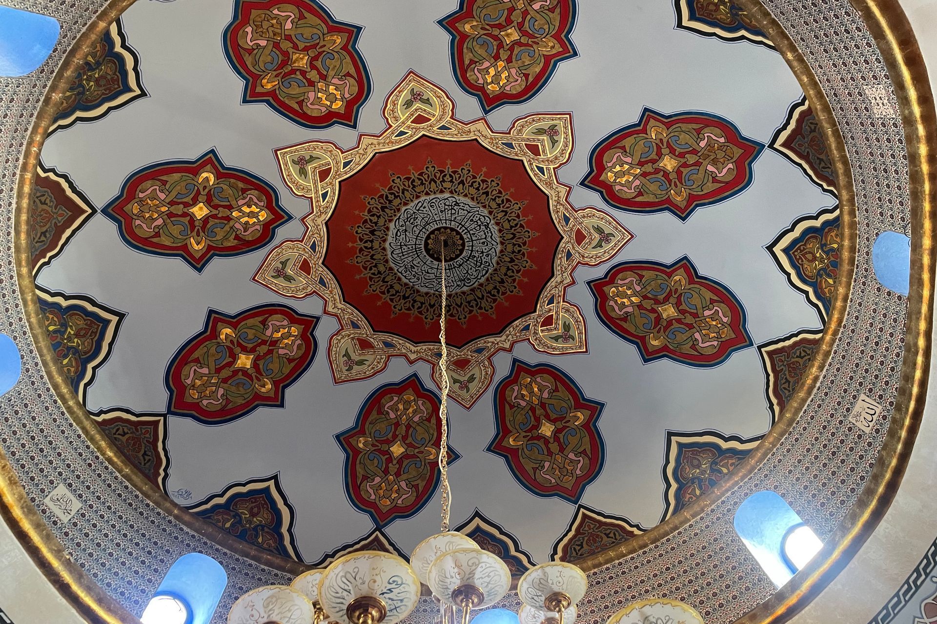Ornate dome ceiling with gold, red, and blue designs and a hanging chandelier.