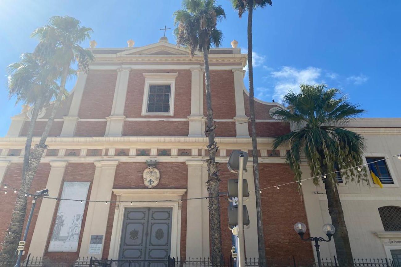 Church exterior with red brick, palm trees, and blue sky.