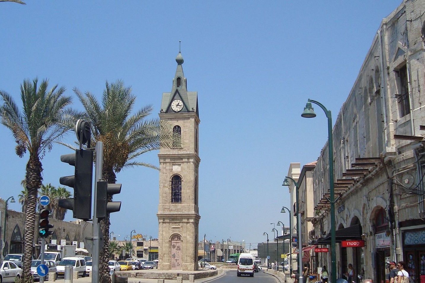 Jaffa Clock Tower in Tel Aviv, Israel, with palm trees, traffic lights, and buildings on a sunny day.