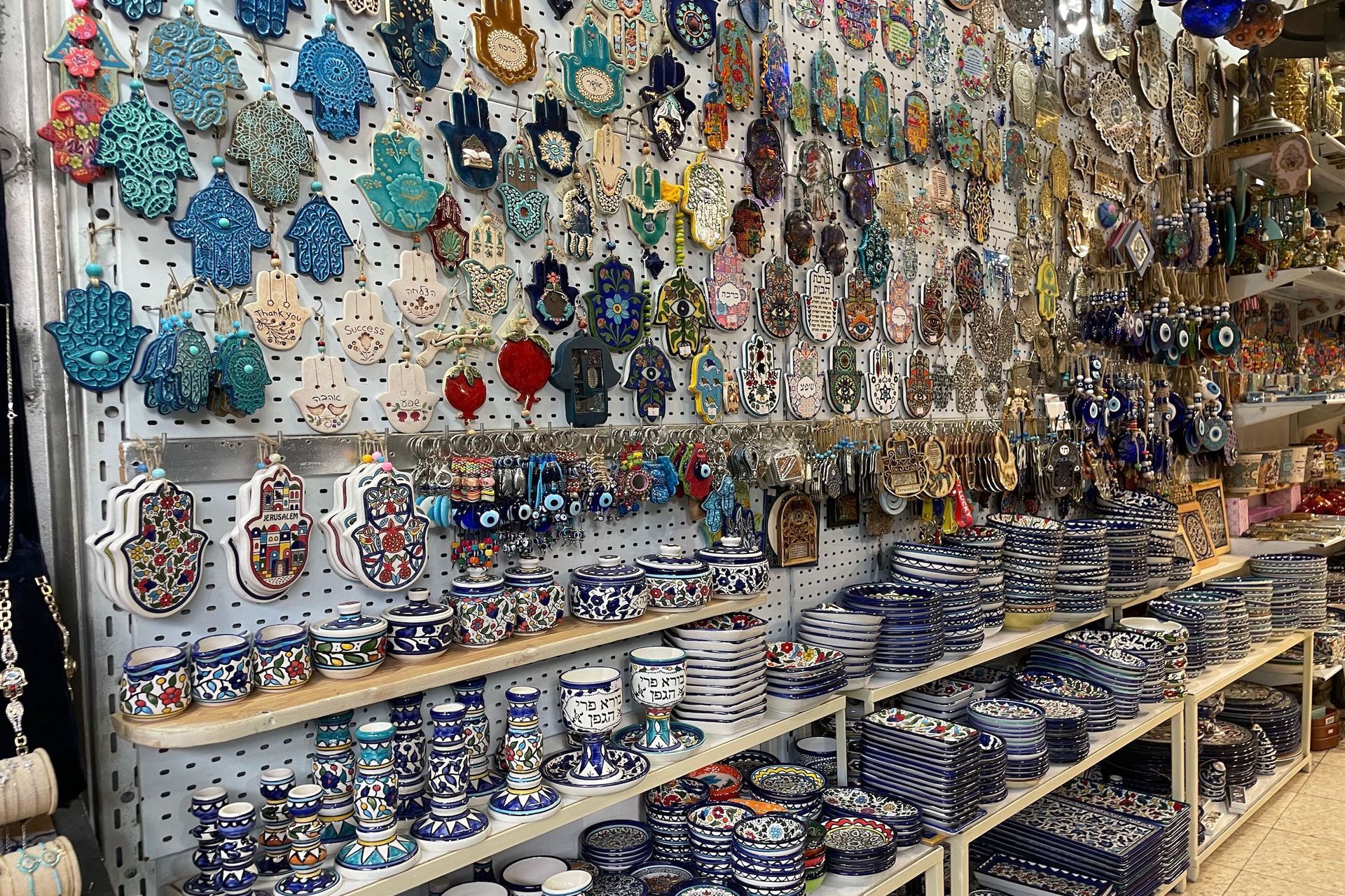 Souvenir shop display: Hamsa hand keychains, blue and white ceramics, various trinkets.