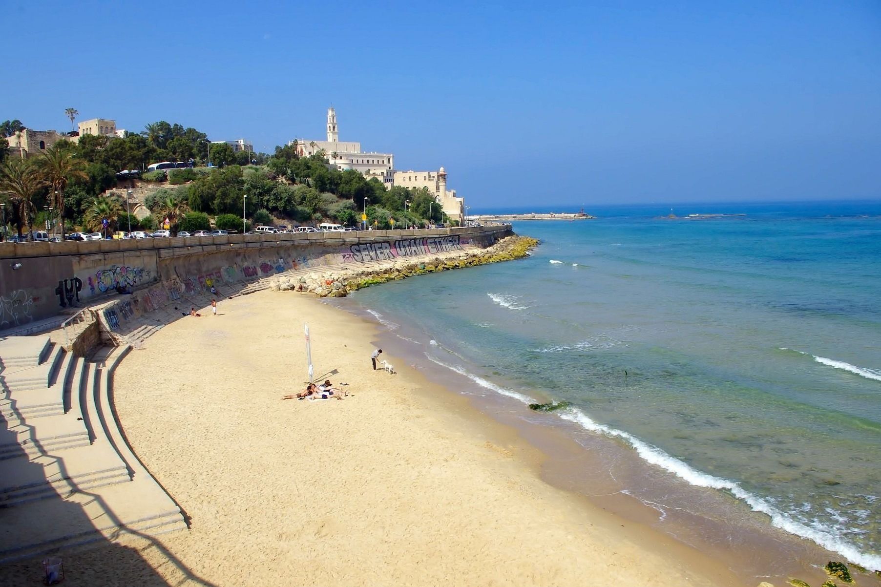 Beach in Jaffa, Israel. Sandy shore with clear turquoise water. Buildings on a cliff in the background.