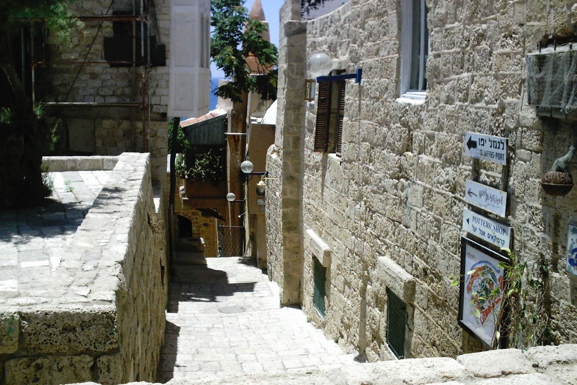 Stone alleyway in sunlight with steps and buildings.