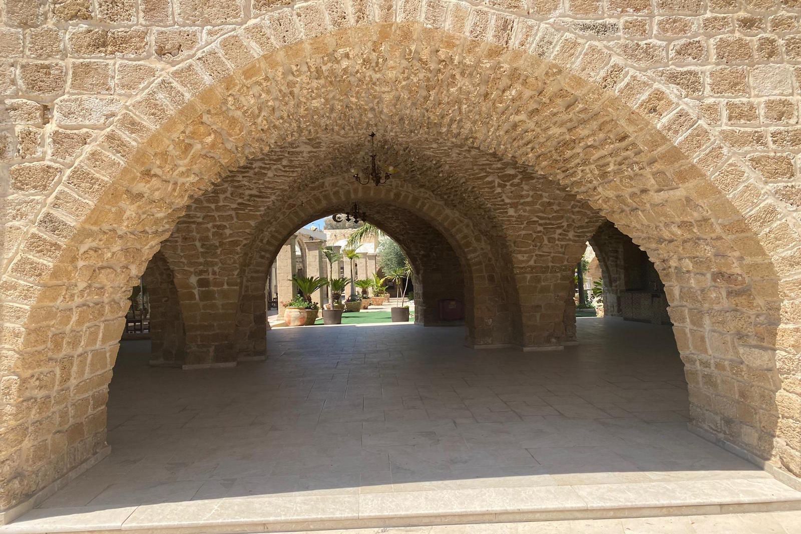 Stone arches leading to an outdoor courtyard with greenery, featuring a textured stone facade.