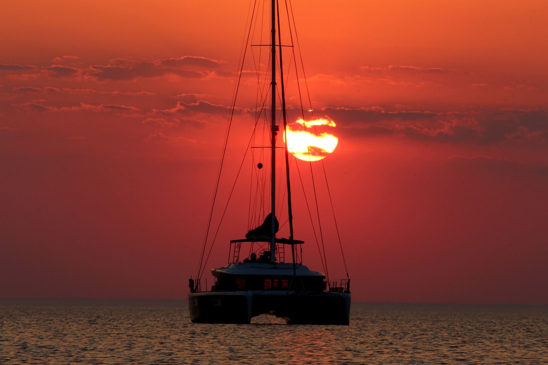 The silouhette of a sailboat with the deep red sunset behind it.