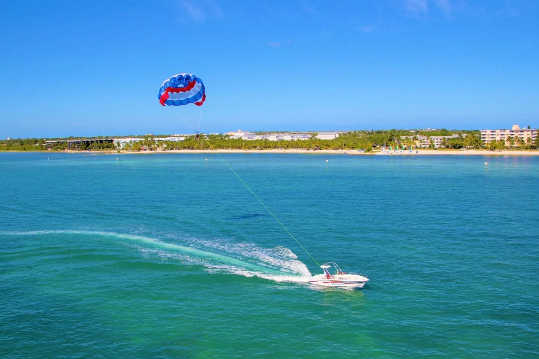 Boat pulling a parasailer over turquoise water under a blue sky.