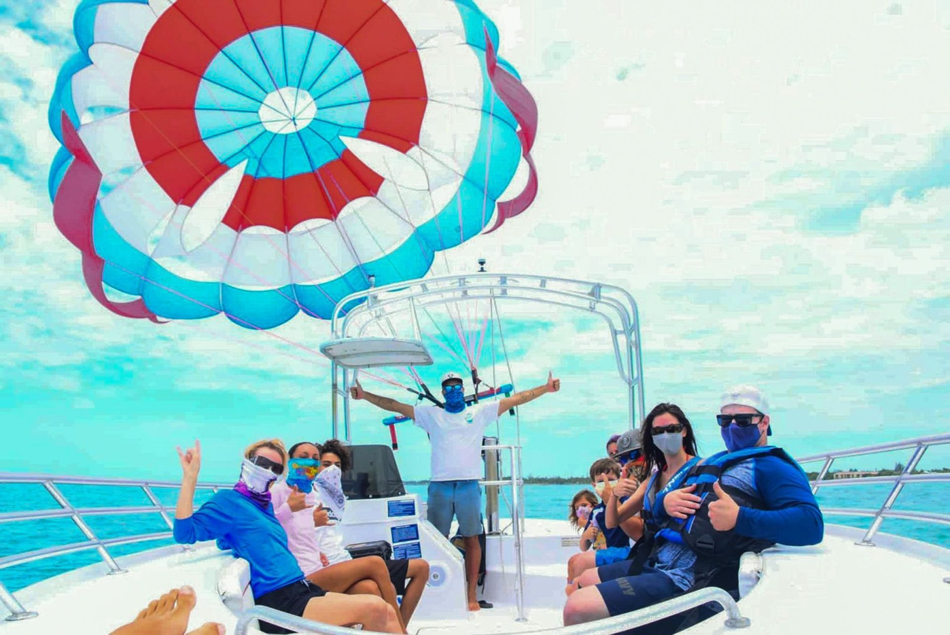 People on a boat parasailing with a red, white, and blue parachute; sunny day.
