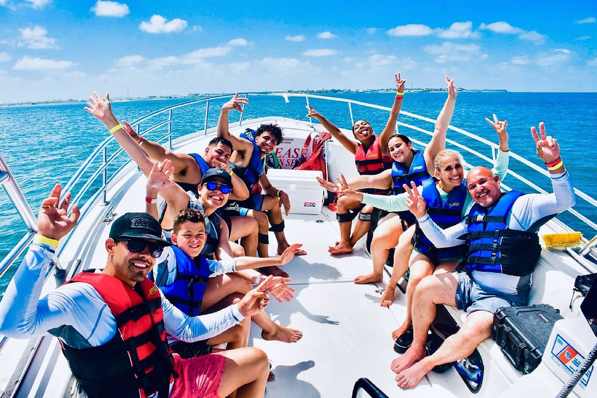 Group of people smiling and waving from a boat on a sunny day.