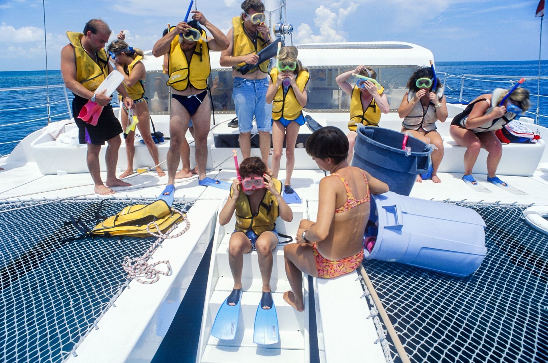 People on a boat, preparing to snorkel. Wearing life vests and masks. Blue water and sky.