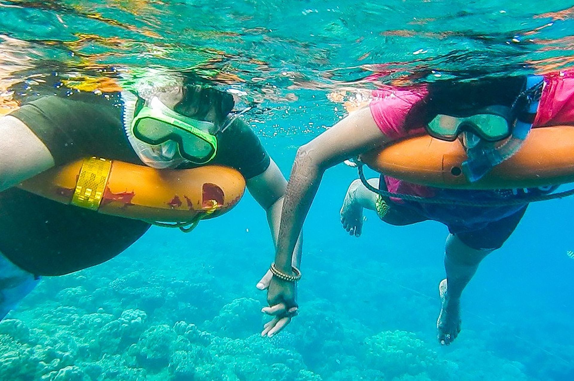 Two snorkelers in blue water, holding hands, wearing masks and life rings.