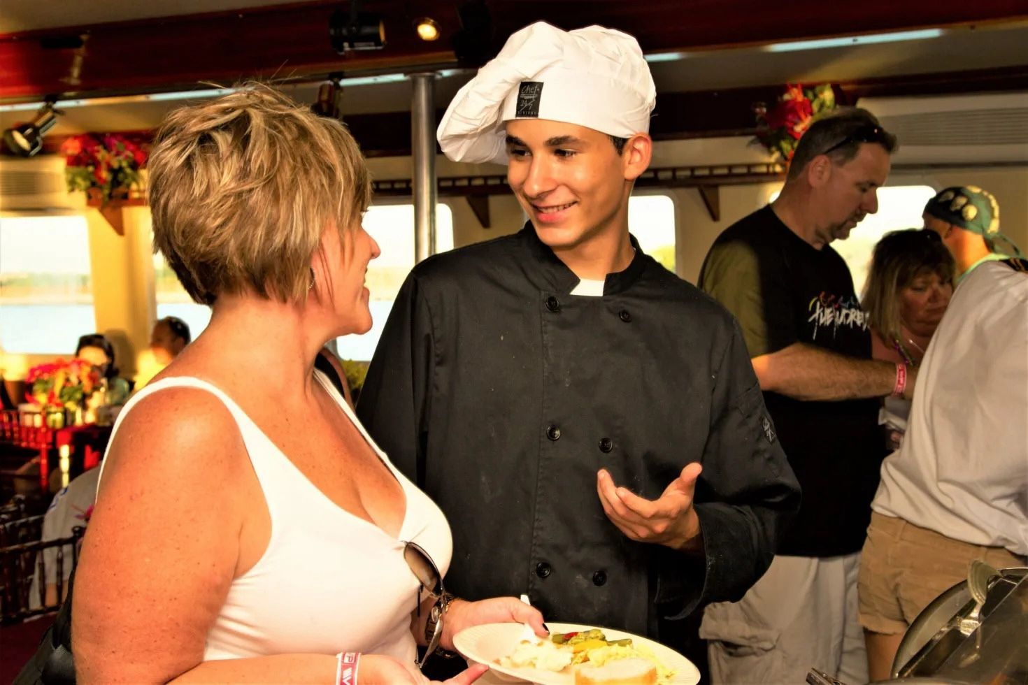 Chef in black jacket talking to a woman at a buffet.