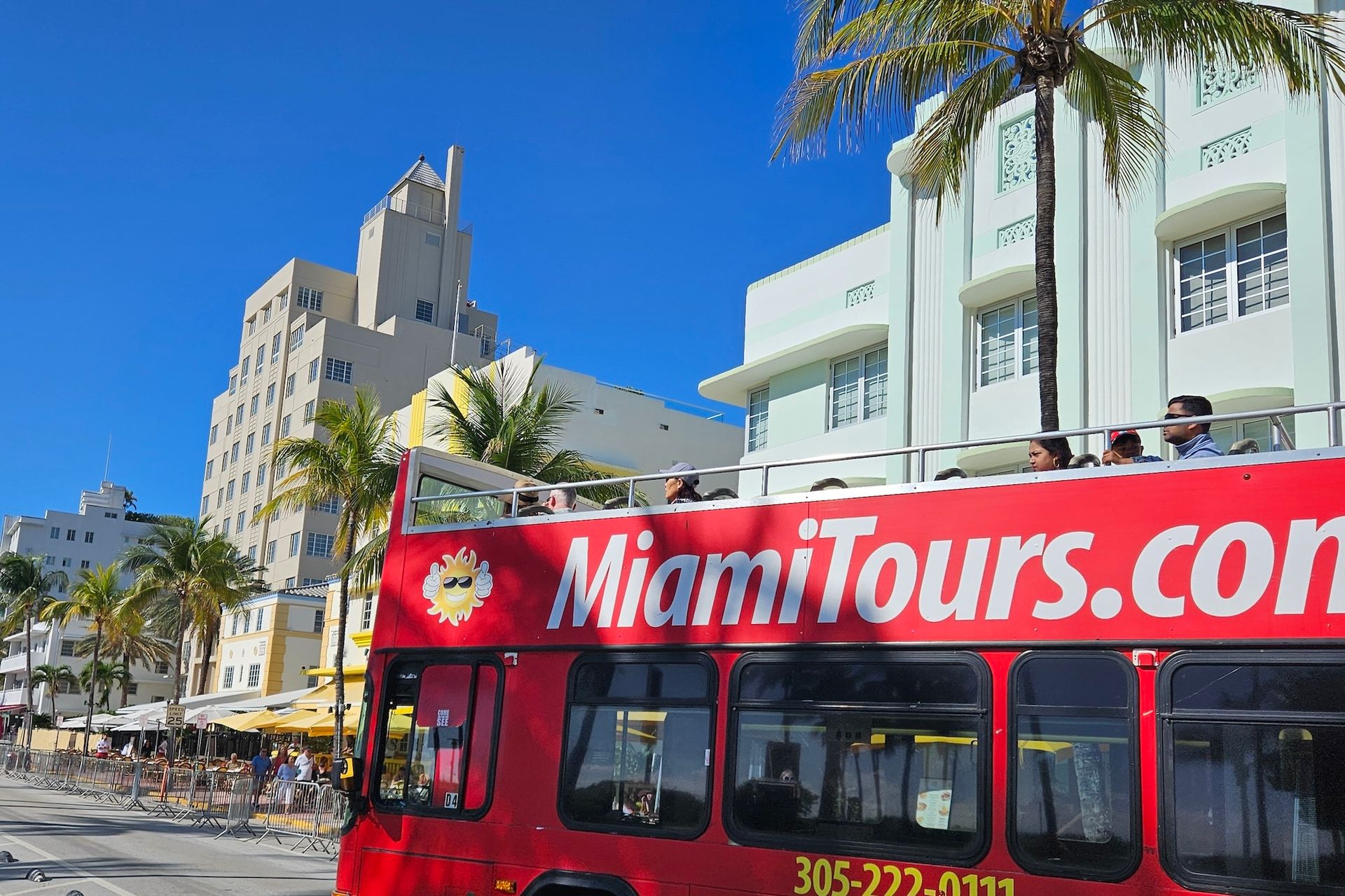 Red Miami Tours double-decker bus on a street in Miami Beach with Art Deco buildings and palm trees.